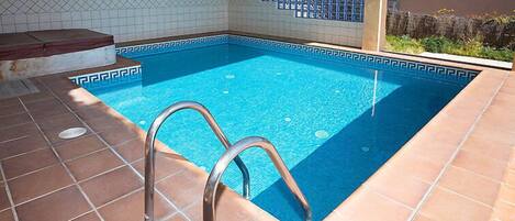 Una piscina con solárium empedrado y escalera metálica.