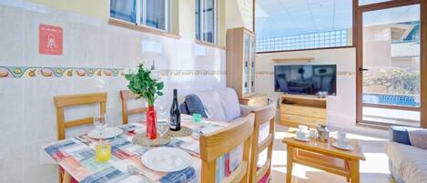 A dining area with a table set for two, a sofa, and a TV in the background.