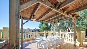 A covered outdoor patio with a tiled floor and white chairs, overlooking a residential area with trees and buildings. - Apartment Raquel by Interhome (Calpe/Calp)