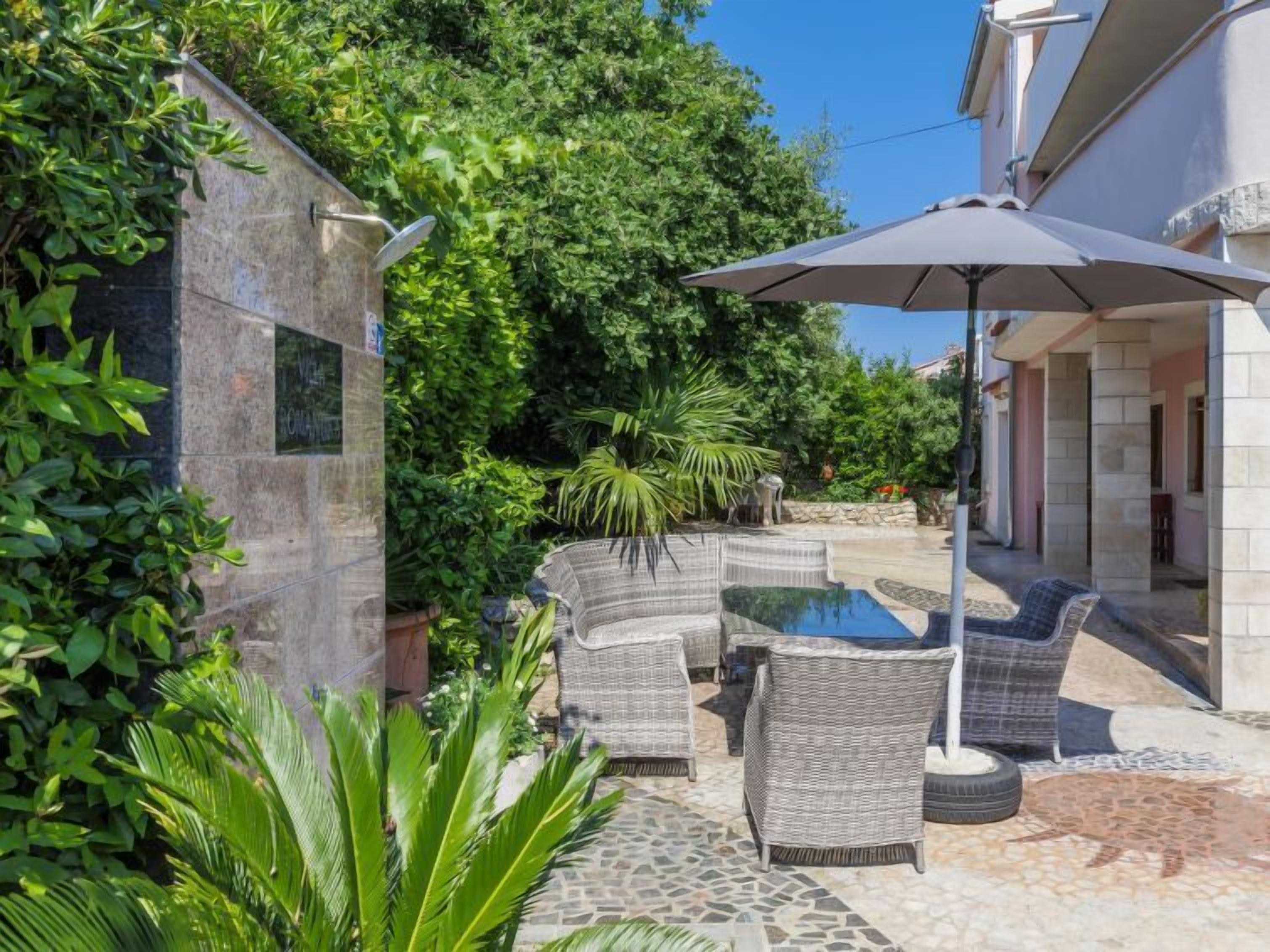 A patio area with wicker furniture, a pool, and lush greenery.