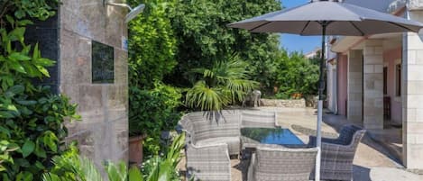 A patio area with wicker furniture, a pool, and lush greenery.
