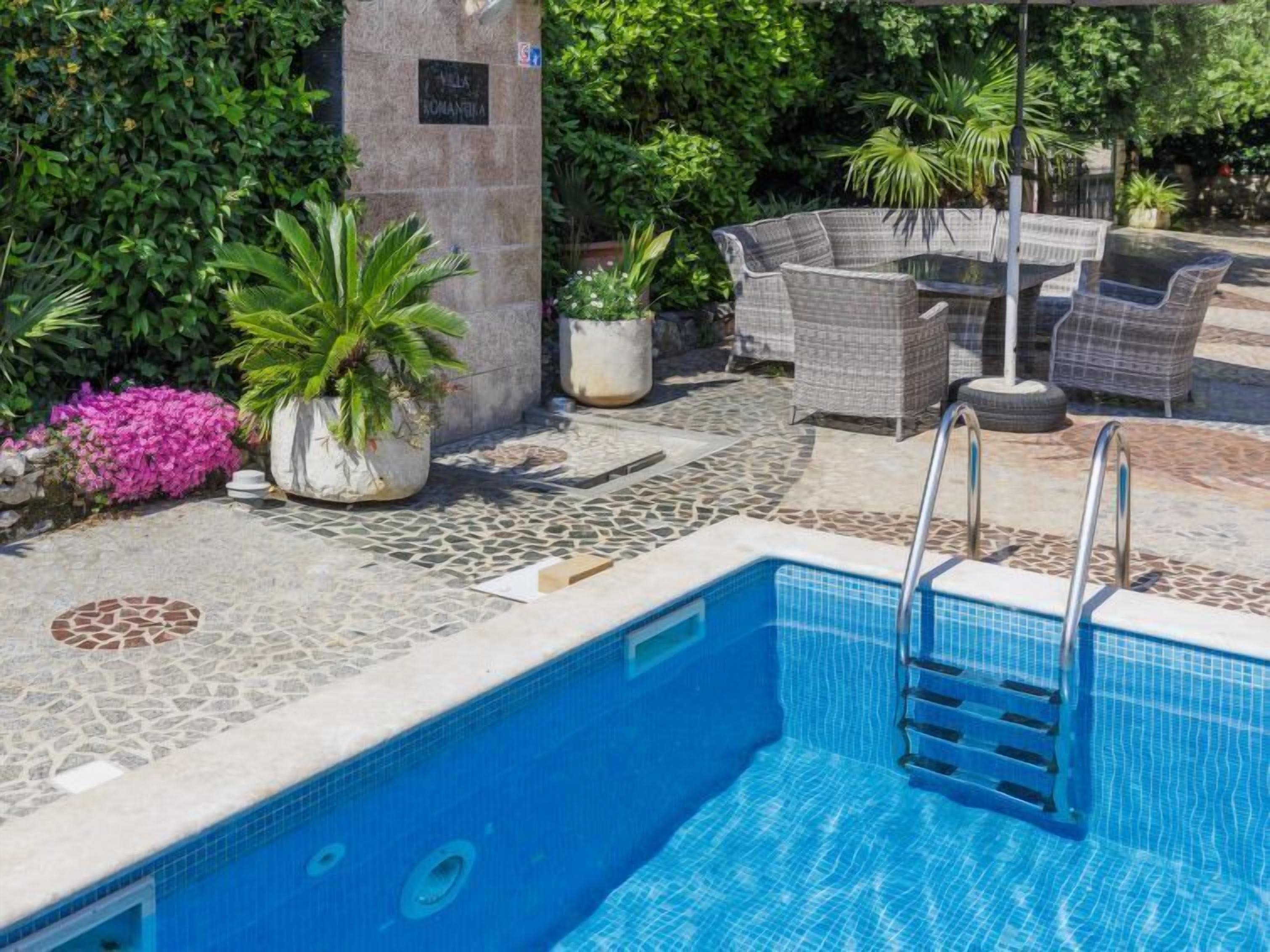 A pool area with a stone-tiled deck, wicker furniture, and potted plants.