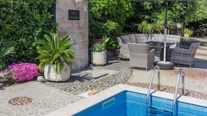 A pool area with a stone-tiled deck, wicker furniture, and potted plants. - Romantika by Interhome (Rovinj)