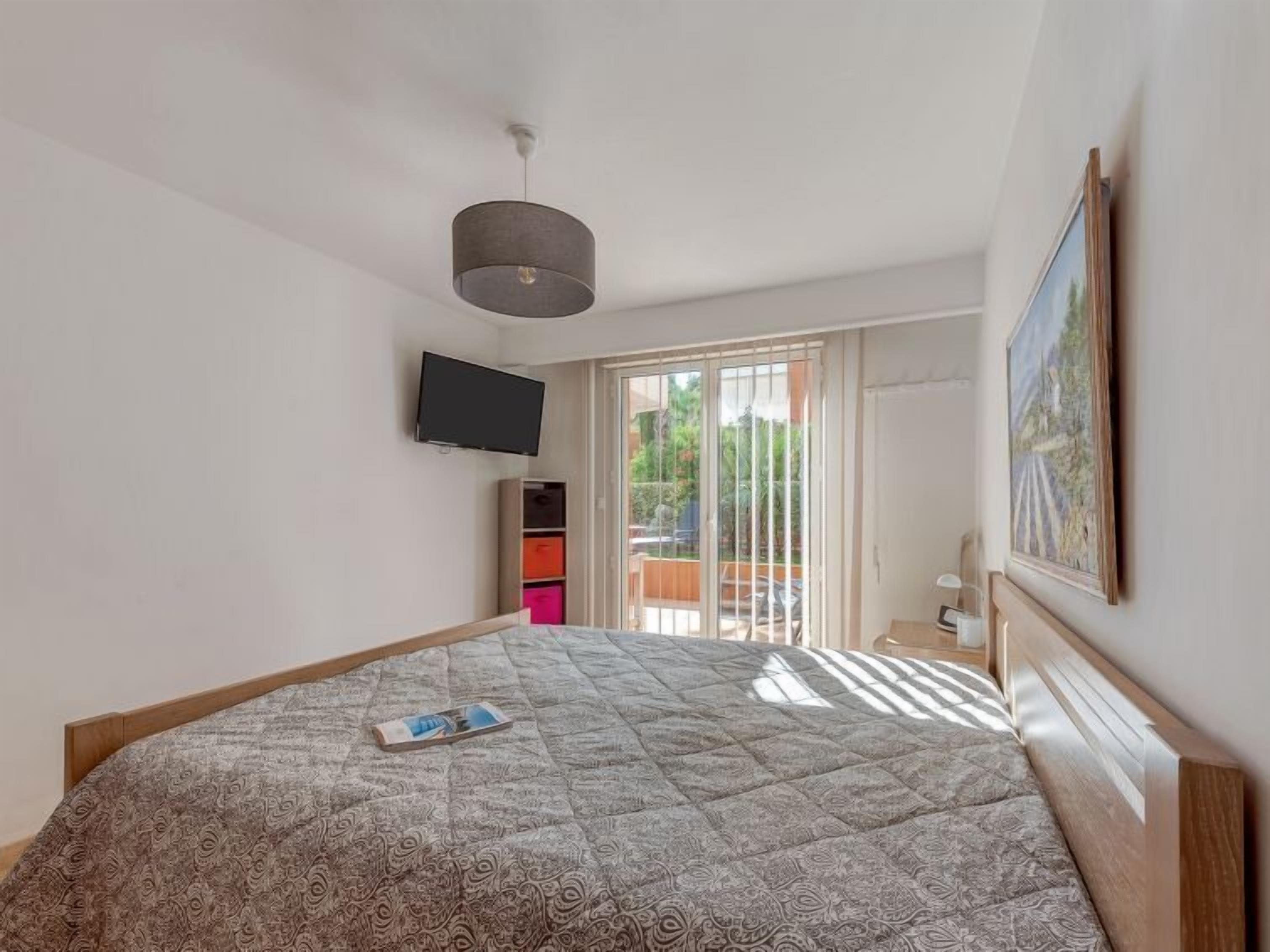 A bedroom with a bed, a TV, a painting, and a sliding door to a balcony.