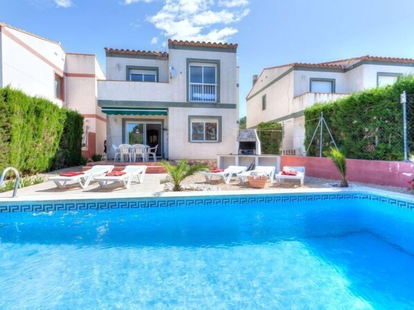 A two-story house with a swimming pool, outdoor seating, and a barbecue area.