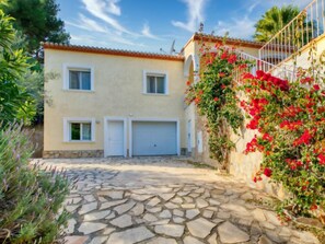 A two-story building with a stone-paved courtyard, a white garage door, and a wall covered with red flowering plants.