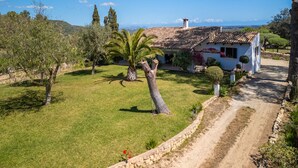 Eine weiße Villa mit Ziegeldach, umgeben von einem gepflegten Rasen und Bäumen, mit freiem Blick auf die Hügel im Hintergrund.
