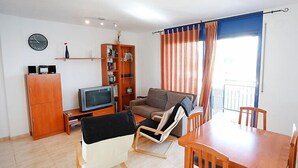 A living room with a sofa, a TV, a bookshelf, a dining table, and a chair. - Vacation home Minini by Interhome (L'Ampolla)