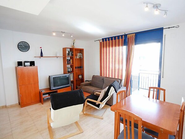 A living room with a sofa, a TV, a bookshelf, a dining table, and a chair.