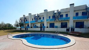 A swimming pool with a hexagonal tiled deck, surrounded by a building with blue balconies and spiral staircases. - Vacation home Minini by Interhome (L'Ampolla)