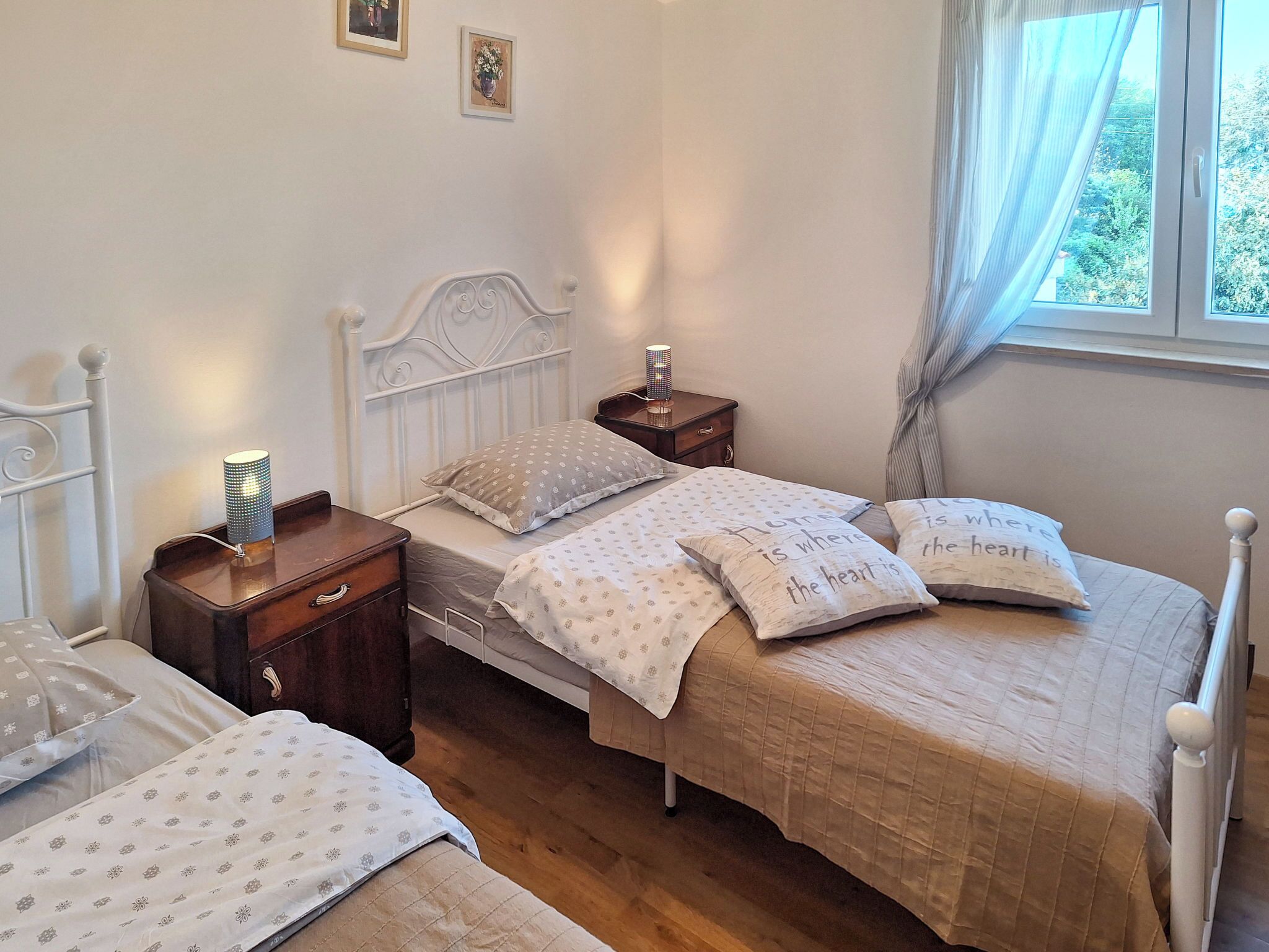 Un dormitorio con dos camas individuales, una mesita de noche con lámpara y cortinas en la ventana.