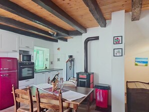 A kitchen with a red refrigerator, a microwave, and an oven. There is a dining table with chairs and a bottle of wine.