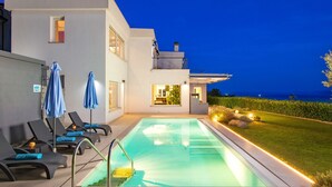 A modern poolside area with lounge chairs and umbrellas, a clear pool, and a view of the sea at dusk. - Vacation home Vista by Interhome (Opatija/Matulji)