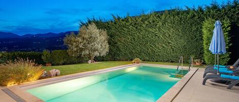 A rectangular swimming pool with a tiled edge, surrounded by a well-maintained lawn and a dense hedge.