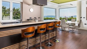A modern kitchen with a large island, bar stools, and a dining area with a view of the sea. - Vacation home Vista by Interhome (Opatija/Matulji)