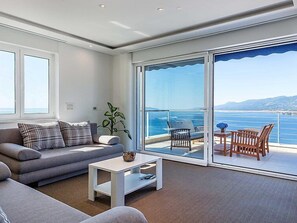 Un salón moderno con sofá, mesa de centro y vista al mar a través de grandes puertas correderas de cristal.