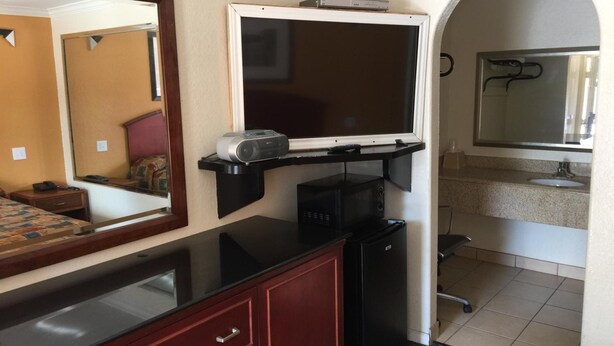 Ett hotellrum med en säng, ett skrivbord, en spegel, en platt-TV, en kaffemaskin, ett kylskåp, ett handfat och en dusch.