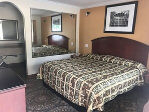 A hotel room with a bed, a desk, a mirror, and a framed picture on the wall. - Regency Inn and Suites (Houston)