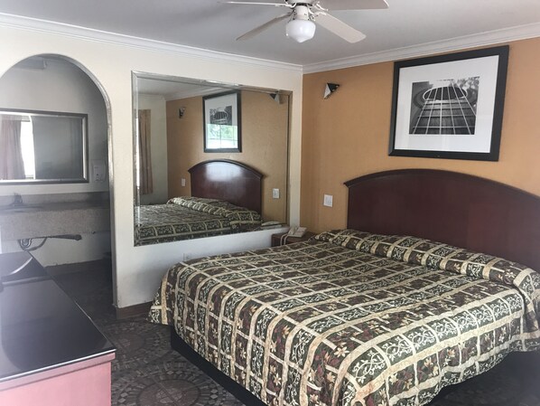 A hotel room with a bed, a desk, a mirror, and a ceiling fan. - Regency Inn and Suites (Houston)