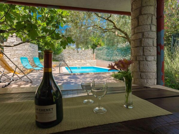 A bottle of wine, two glasses, and a vase with flowers on a table by a poolside.