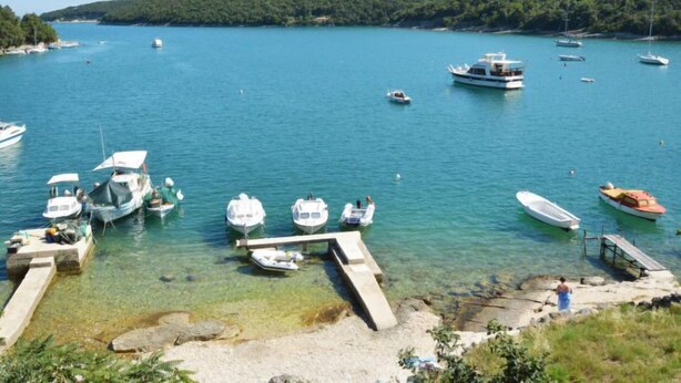 Una marina con varios barcos amarrados, agua cristalina y un paisaje montañoso al fondo.