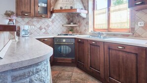 Una cocina con armarios de madera oscura, salpicadero de piedra, horno empotrado y ventana con vistas a zonas verdes.