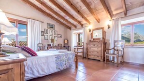 Een slaapkamer met een bed, een houten dressoir, stoelen en een raam met uitzicht op bergen.
