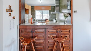Une cuisine avec des meubles en bois, un îlot central doté de tabourets, une fenêtre offrant une belle vue et une hotte de cuisine en acier inoxydable.