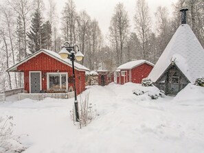 A red cabin with a snow-covered roof, surrounded by a snowy landscape and trees.