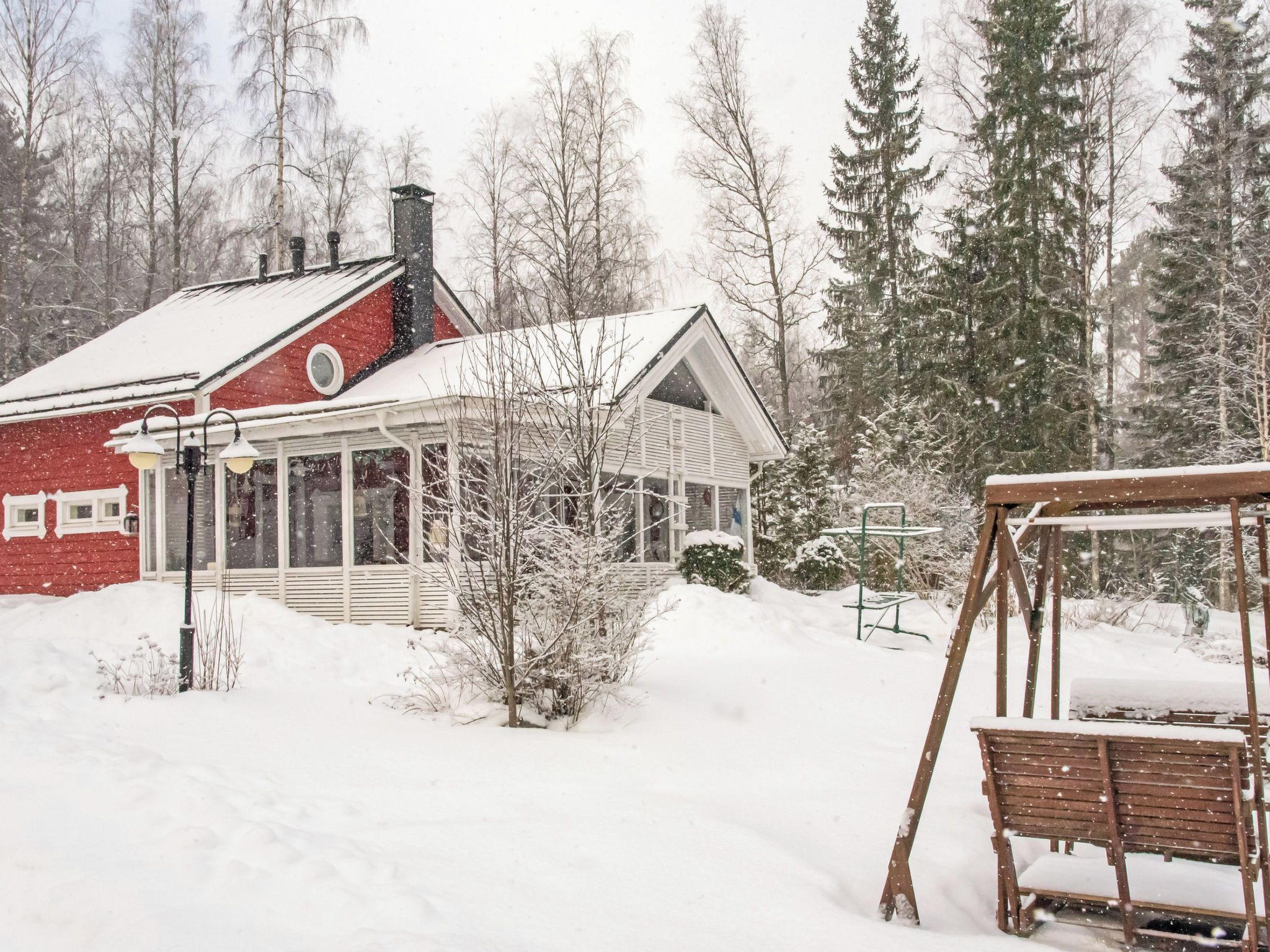 A snow-covered house with a red exterior, a porch, and a swing set in the foreground.