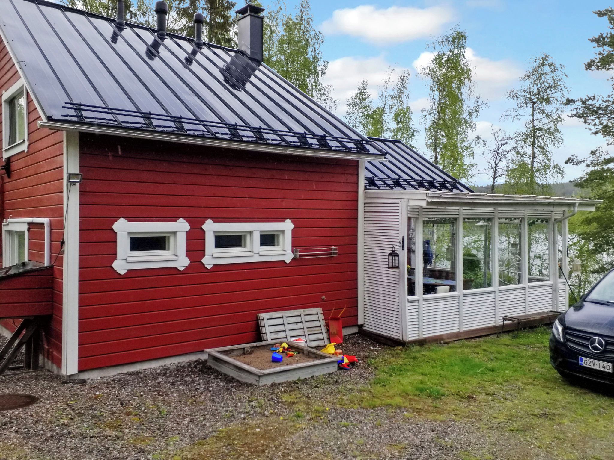 A red house with a metal roof, a small deck, and a car parked in front.