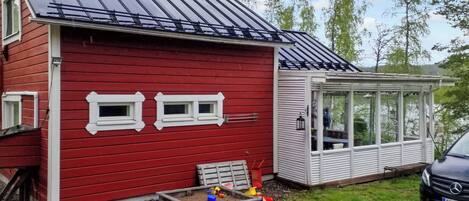 A red house with a metal roof, a small deck, and a car parked in front.