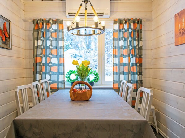 A dining room with a table set for four, a chandelier, and curtains with a geometric pattern.