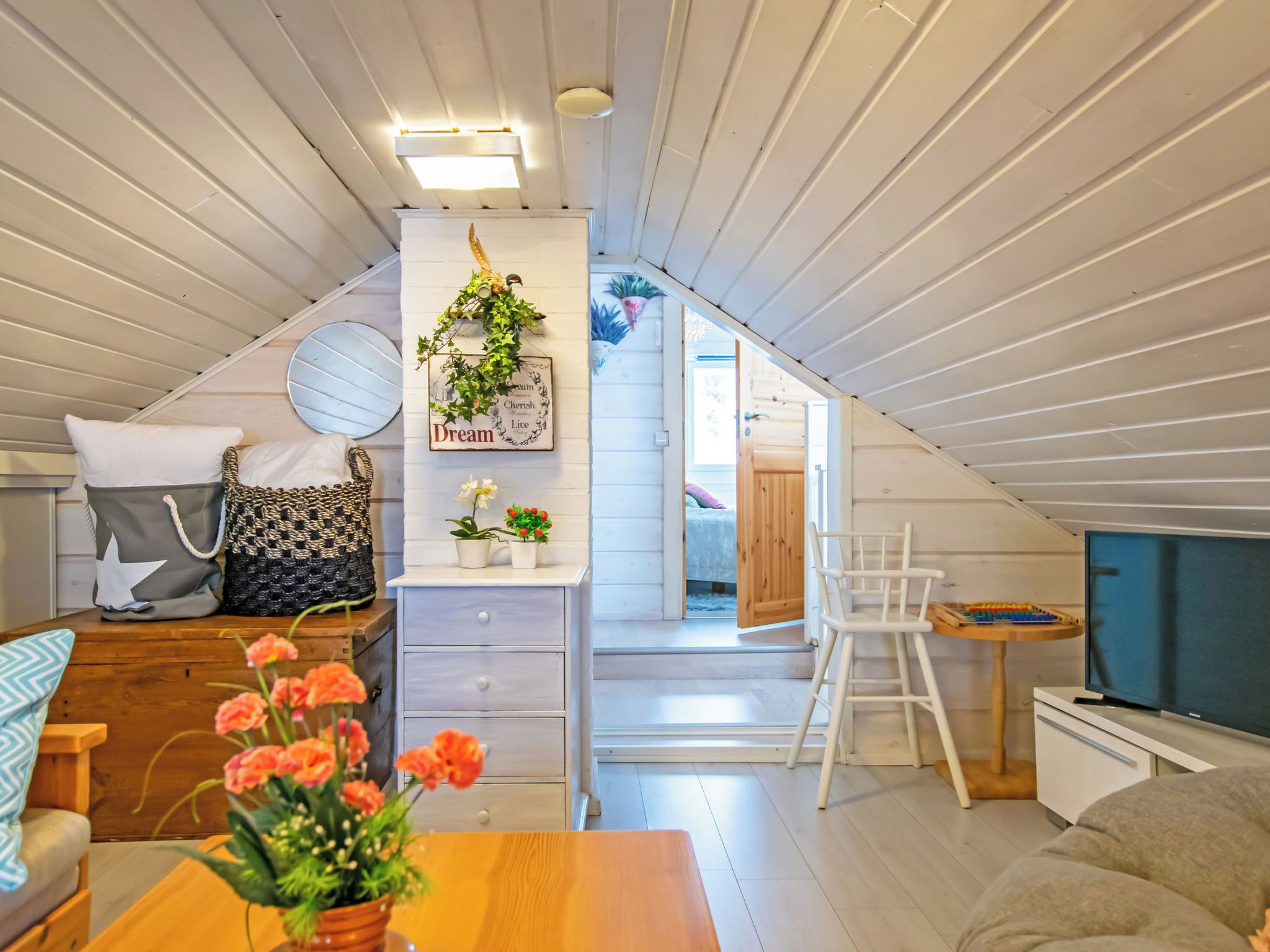 Ein gemütliches Schlafzimmer im Dachgeschoss mit schrägen Wänden, einem Bett, einem Schminktisch, einem Sessel und einem Fernseher.