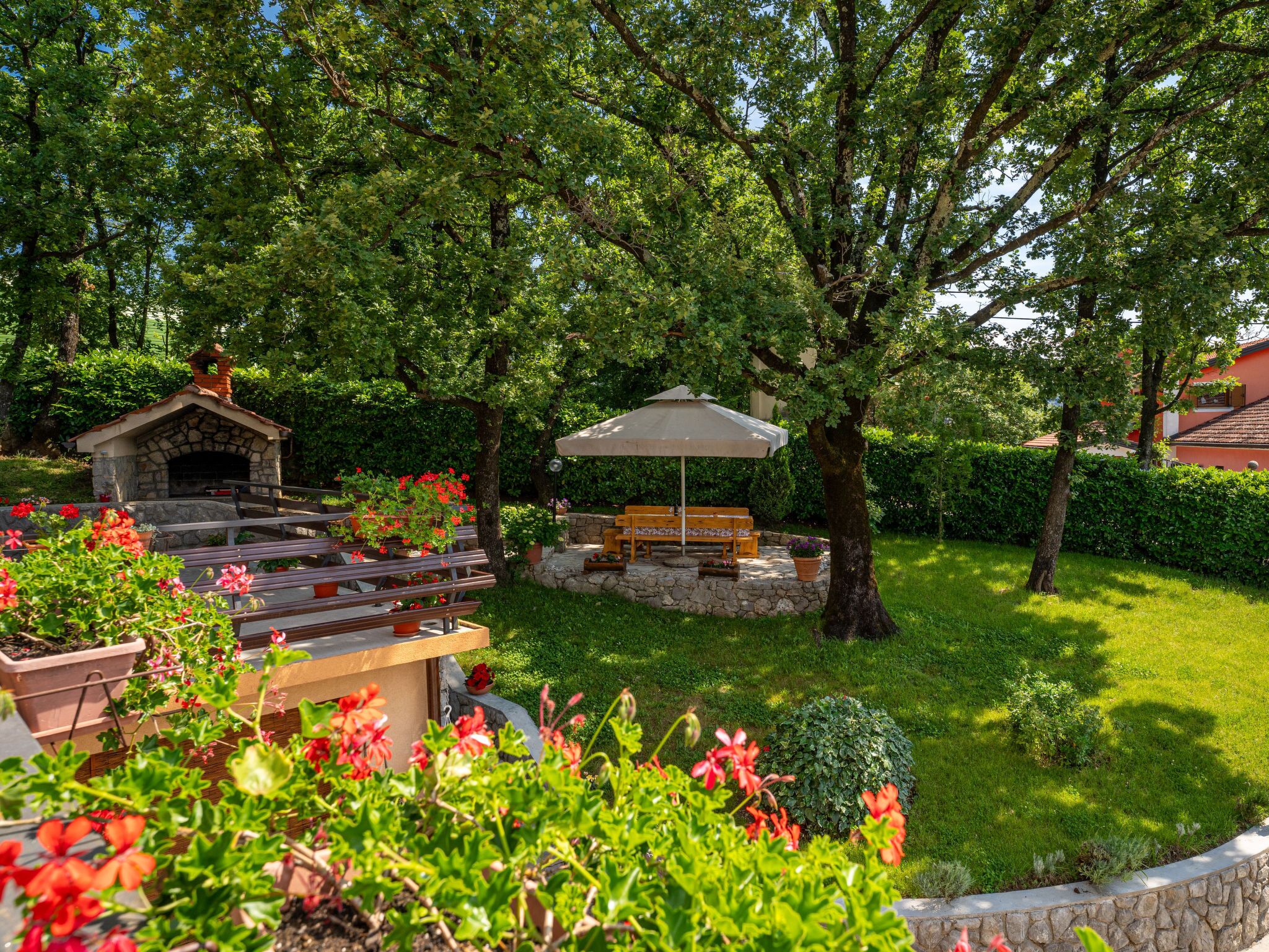 Un jardín con una cocina al aire libre de piedra, un banco de madera y un paraguas grande.
