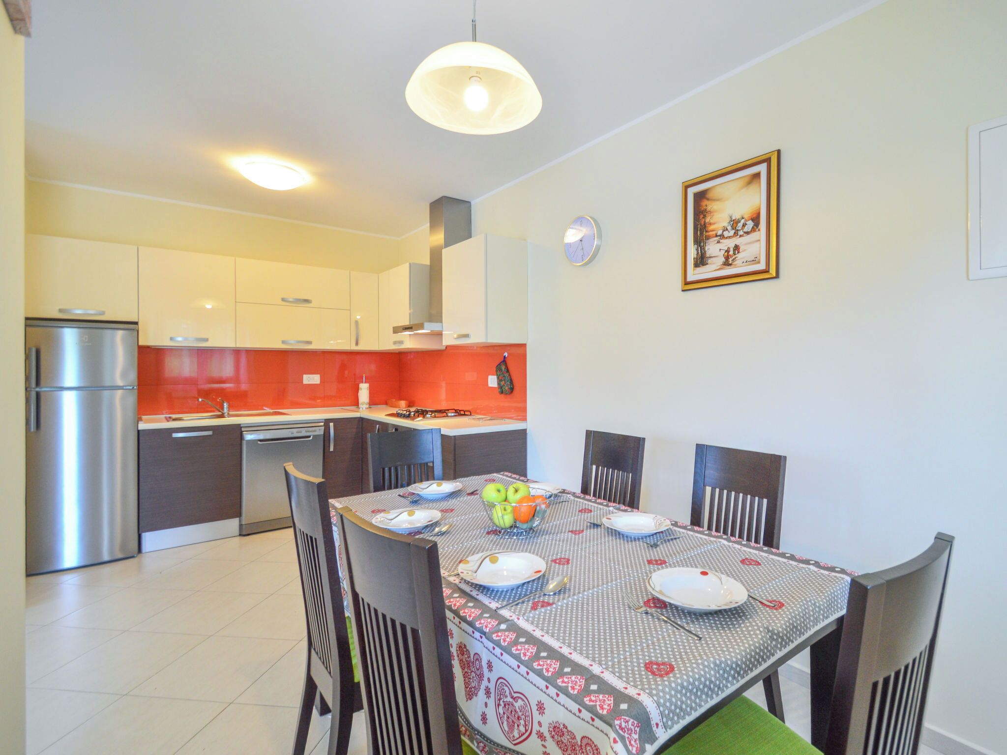 Une cuisine moderne avec des meubles blancs, un pare-feu rouge et un coin repas avec une table dressée pour quatre personnes.