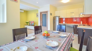 A dining area with a table set for four, a kitchen with modern appliances, and a yellow accent wall. - Apartment Marijo by Interhome (Opatija/Matulji)