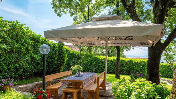 An outdoor patio with a table and benches under a Coca-Cola branded umbrella, surrounded by greenery and a stone pathway. - Apartment Marijo by Interhome (Opatija/Matulji)