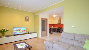 A living room with a sofa, a coffee table, and a TV. There is a kitchen visible through an open doorway. - Apartment Marijo by Interhome (Opatija/Matulji)