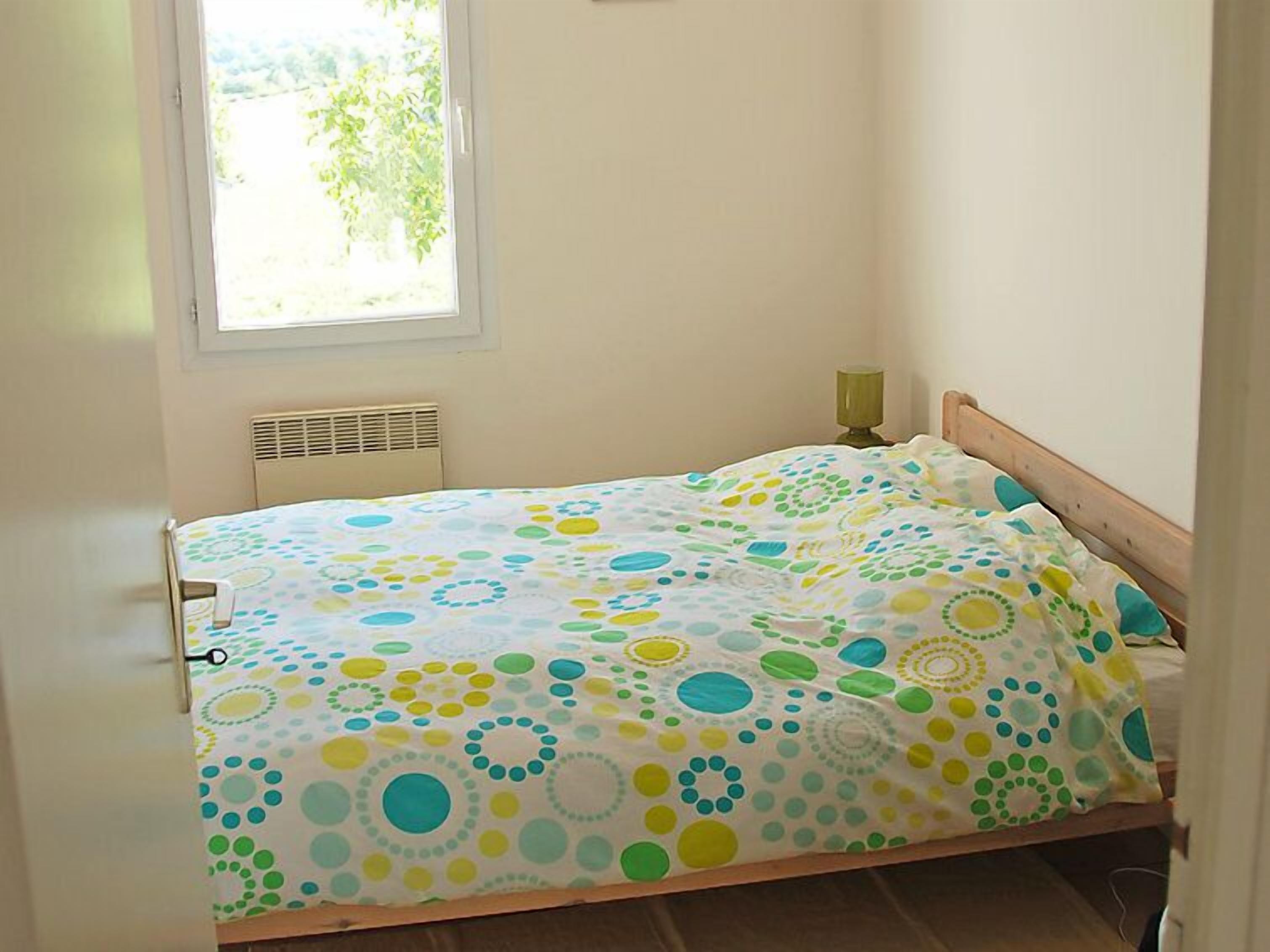 A small, single-bed room with a window, a radiator, and a bedside table with a lamp.