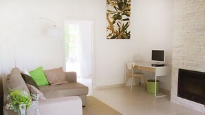 Una sala de estar moderna con un sofá blanco, una pequeña mesa con jarrones, un escritorio con una computadora y una chimenea.