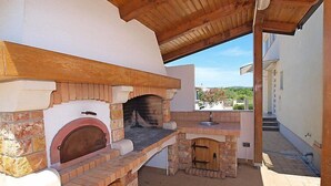 An outdoor kitchen with a brick oven and a sink, under a wooden roof. - Apartment Sablić by Interhome (Pirovac)