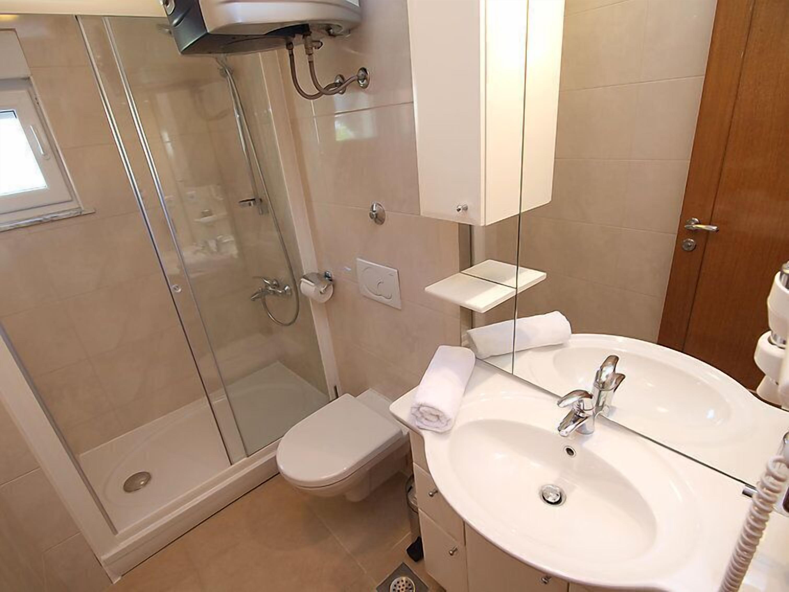 Une salle de bain moderne avec une douche à parois de verre, des toilettes, un lavabo avec un miroir et une petite étagère.