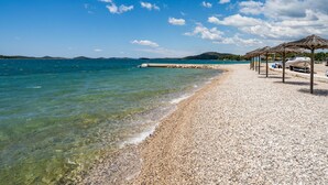 A pebble beach with clear water, a pier, and beach umbrellas. - Apartment Sablić by Interhome (Pirovac)