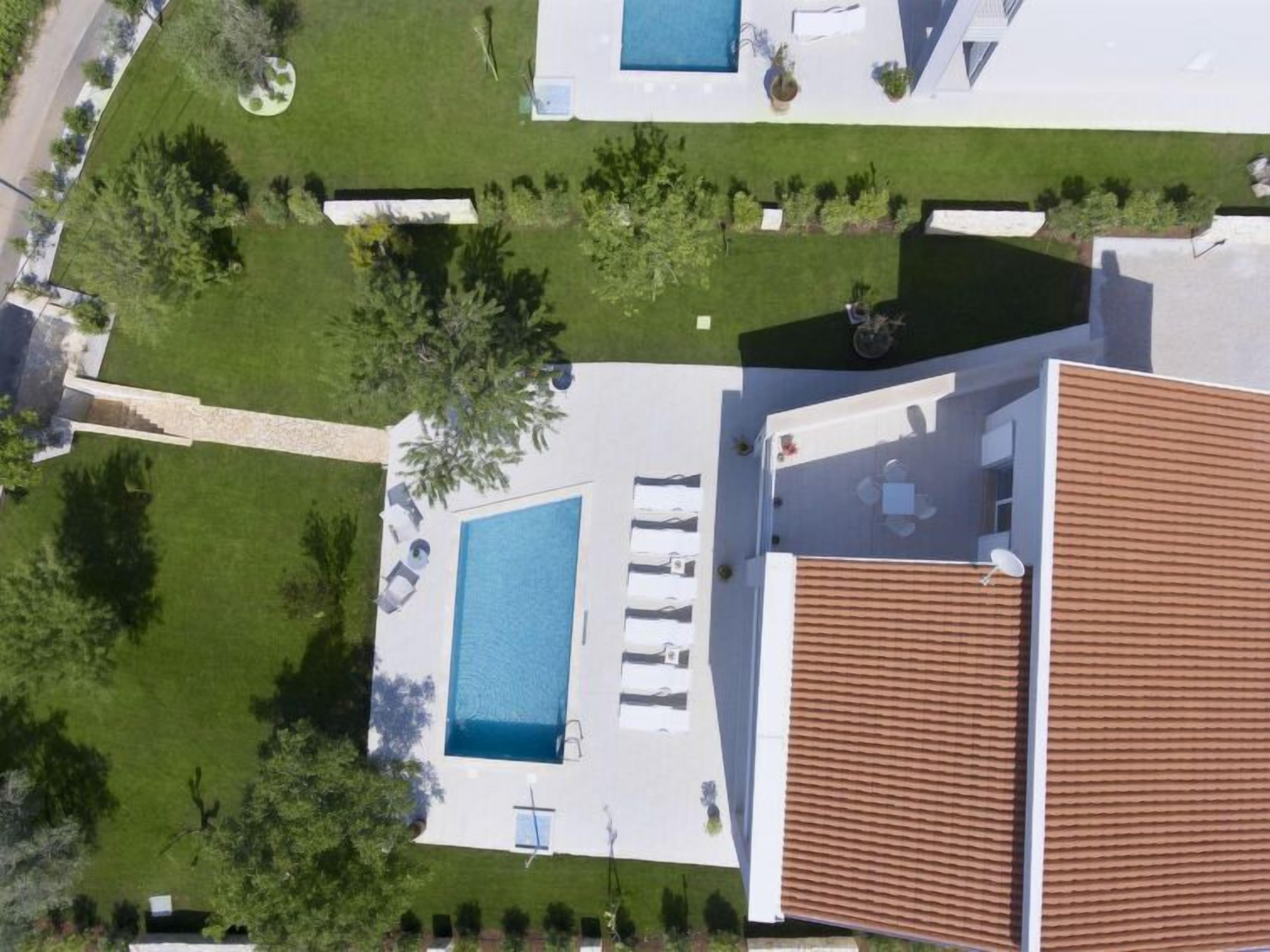 An aerial view of a modern house with a swimming pool, a patio area, and a garden.