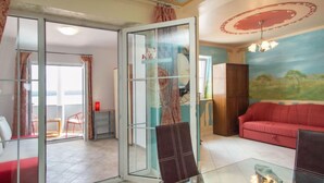 Un salón con separador de vidrio, un sofá rojo, una mesa de centro de vidrio y un cuadro de un paisaje en la pared.