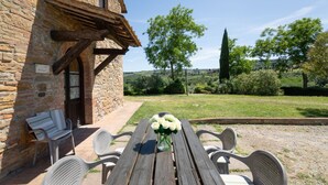 A rustic stone building with a wooden table and chairs, a vase of white flowers, and a view of a green landscape with trees and hills. - Michelangelo by Interhome (Montaione)