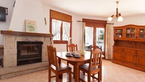 A dining area with a stone fireplace, wooden chairs, a table, and a wooden cabinet. - Villa Zozo by Interhome (L'Ametlla de Mar)