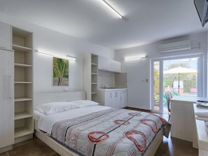Une chambre avec un lit, des étagères intégrées, un bureau et une vue sur une terrasse extérieure.