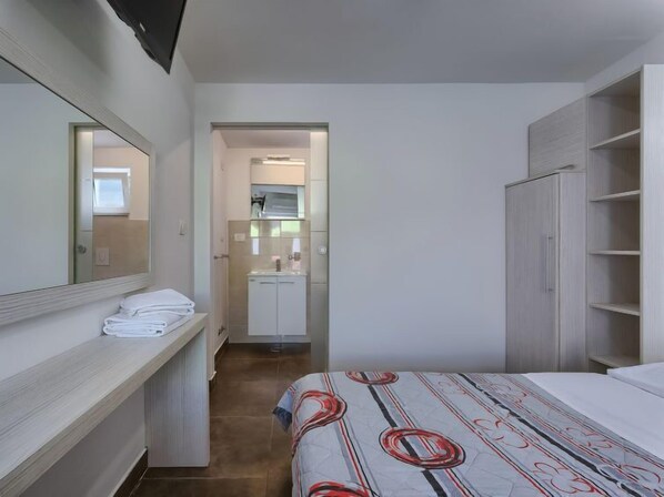 Ein Schlafzimmer mit Bett, Kleiderschrank, Spiegel und einem Badezimmer mit Waschbecken und Handtuchhalter.